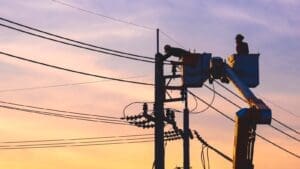 Powerline repair worker in bucket lift working on overhead cables at sunset