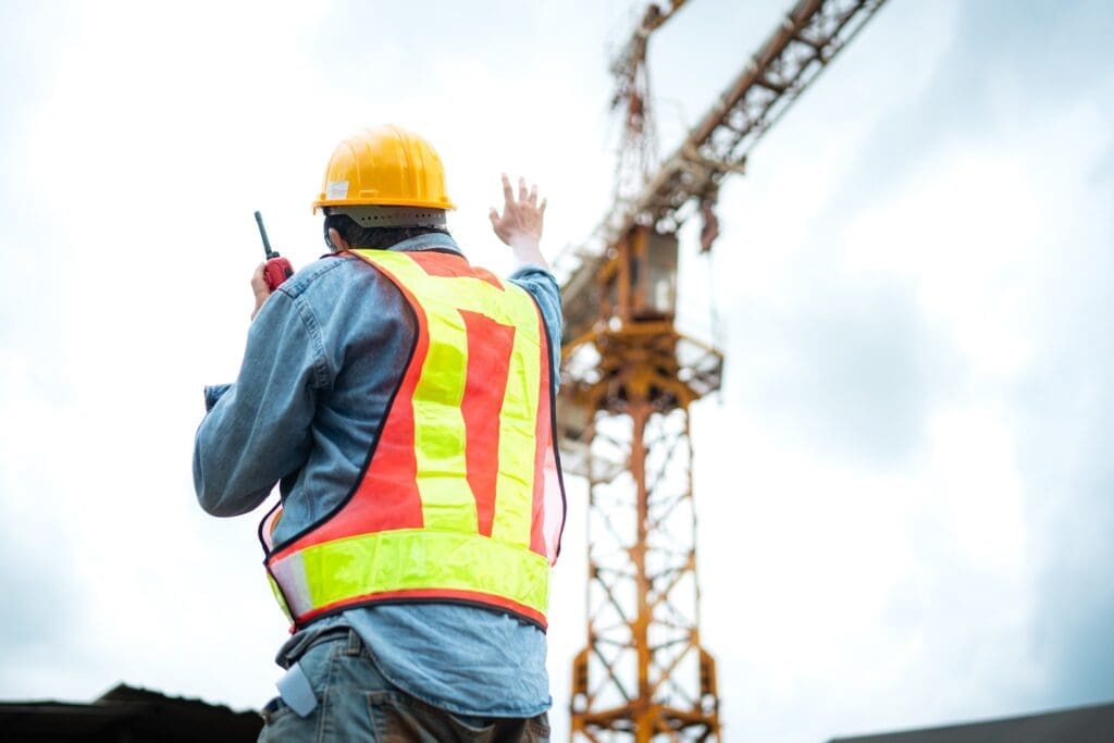 Portrait of crane worker uses OSHA hand signals to communicate with tower crane operators to lift and move objects on building construction sites